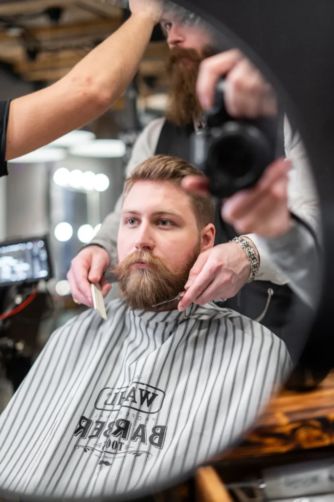 Barber shaping a ginger beard with scissors in a mirror